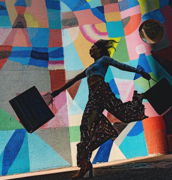 Consumidor feliz caminha em frente mural de arte de rua. Foto: Unsplash