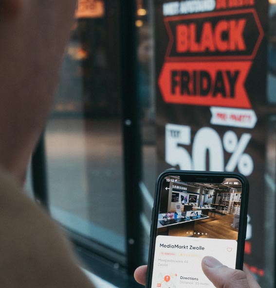 Pessoa segurando smartphone e olhando para cartaz de loja com promoção Black Friday. Comércio eletrônico, compras on-line. Foto: CardMapr/Unsplash